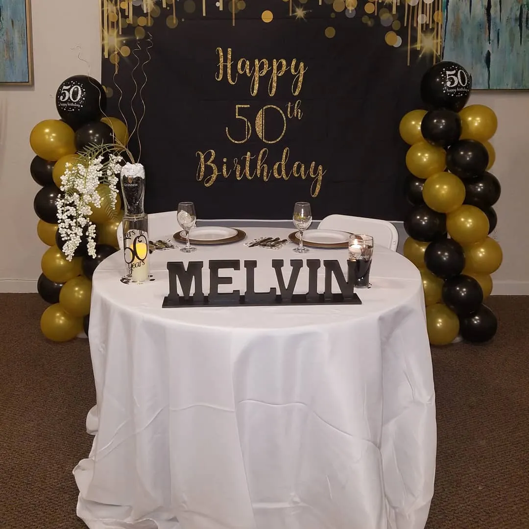 Black and gold 50th birthday sweetheart table with balloon columns and a custom name sign