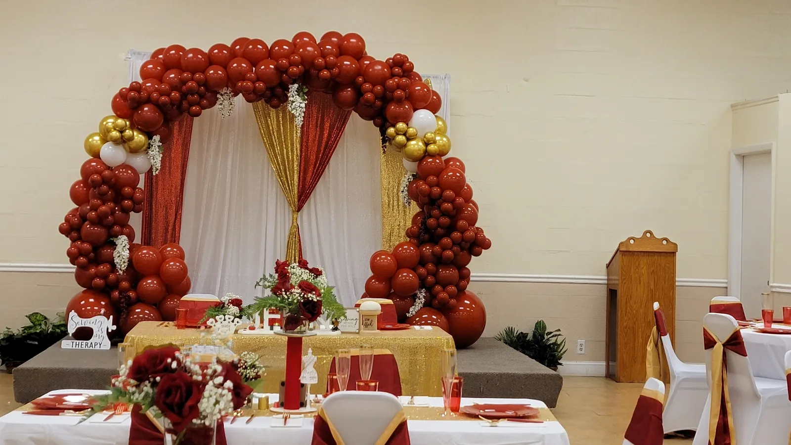 Red, gold and white balloon arch over a sequin-draped sweetheart table for a milestone celebration