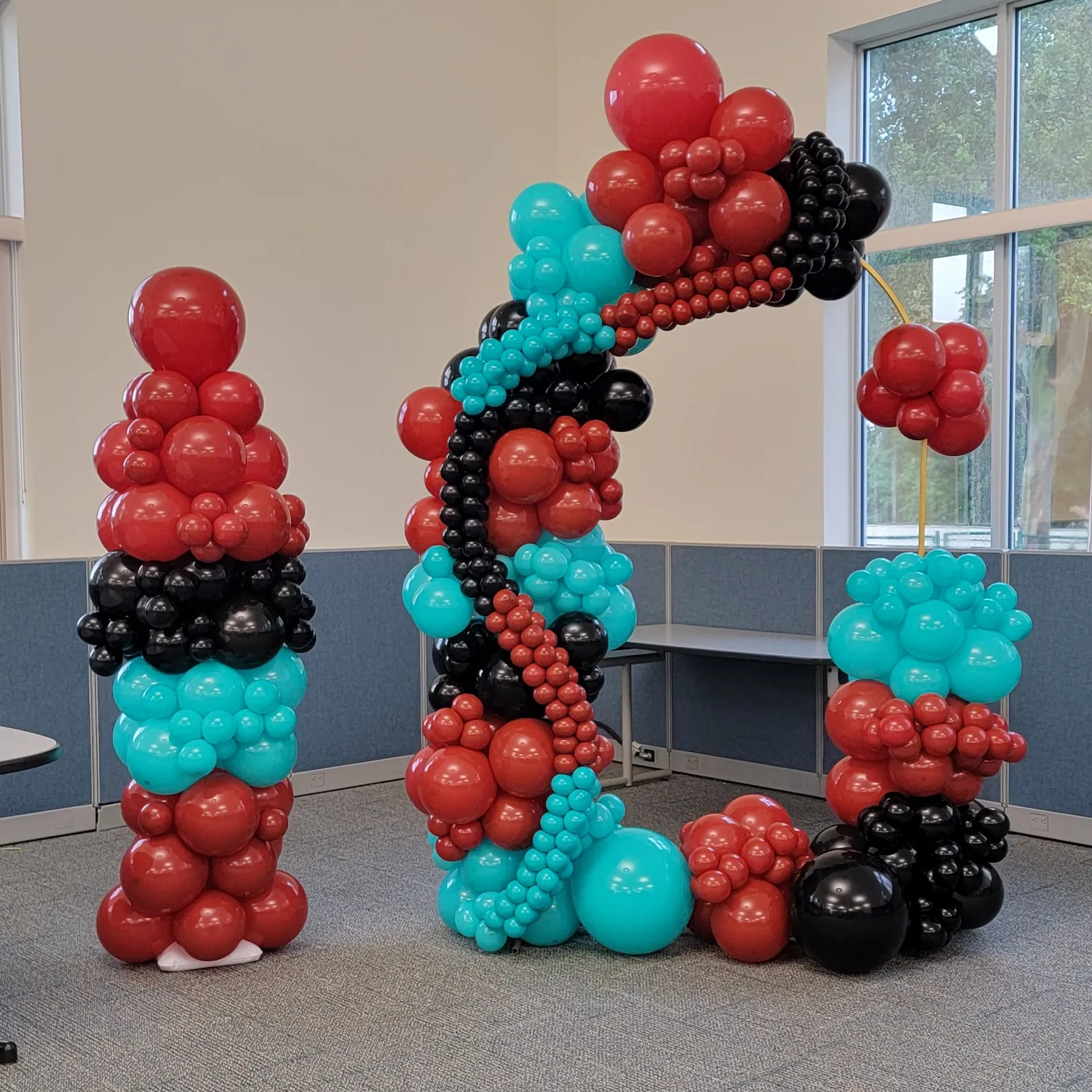Red, teal and black organic balloon arch and matching column installed for an office celebration