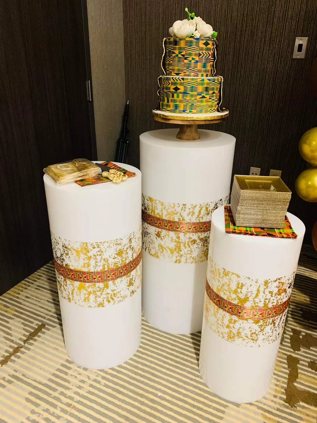 Kente-accented cake display on white and gold pedestals for a Ghanaian celebration